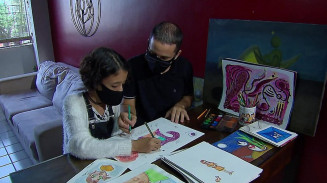 Marina e o pai, André, desenham e criam juntos na sala de casa